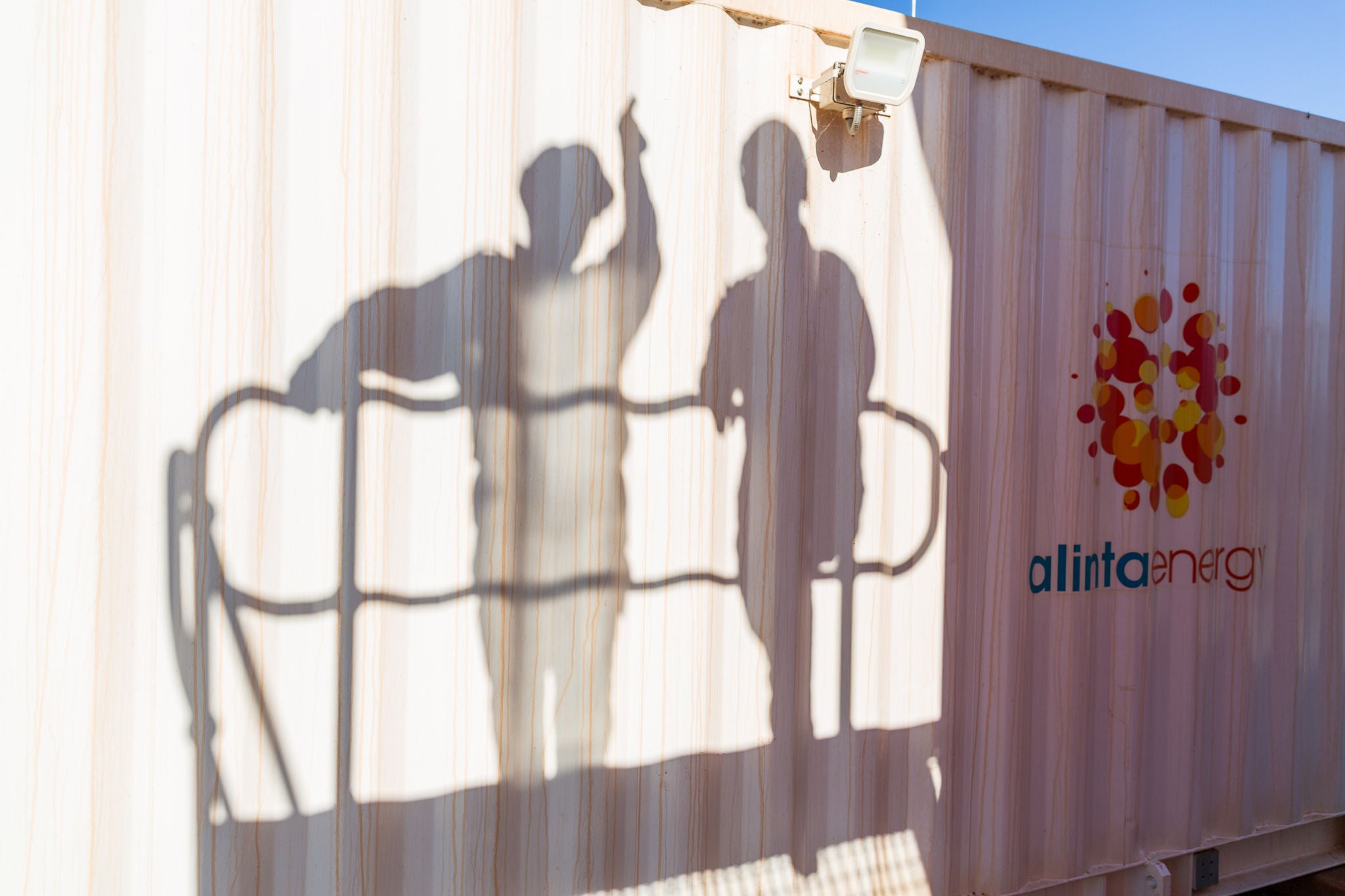 An image of an Alinta Energy container with the shadow of two workers on it.