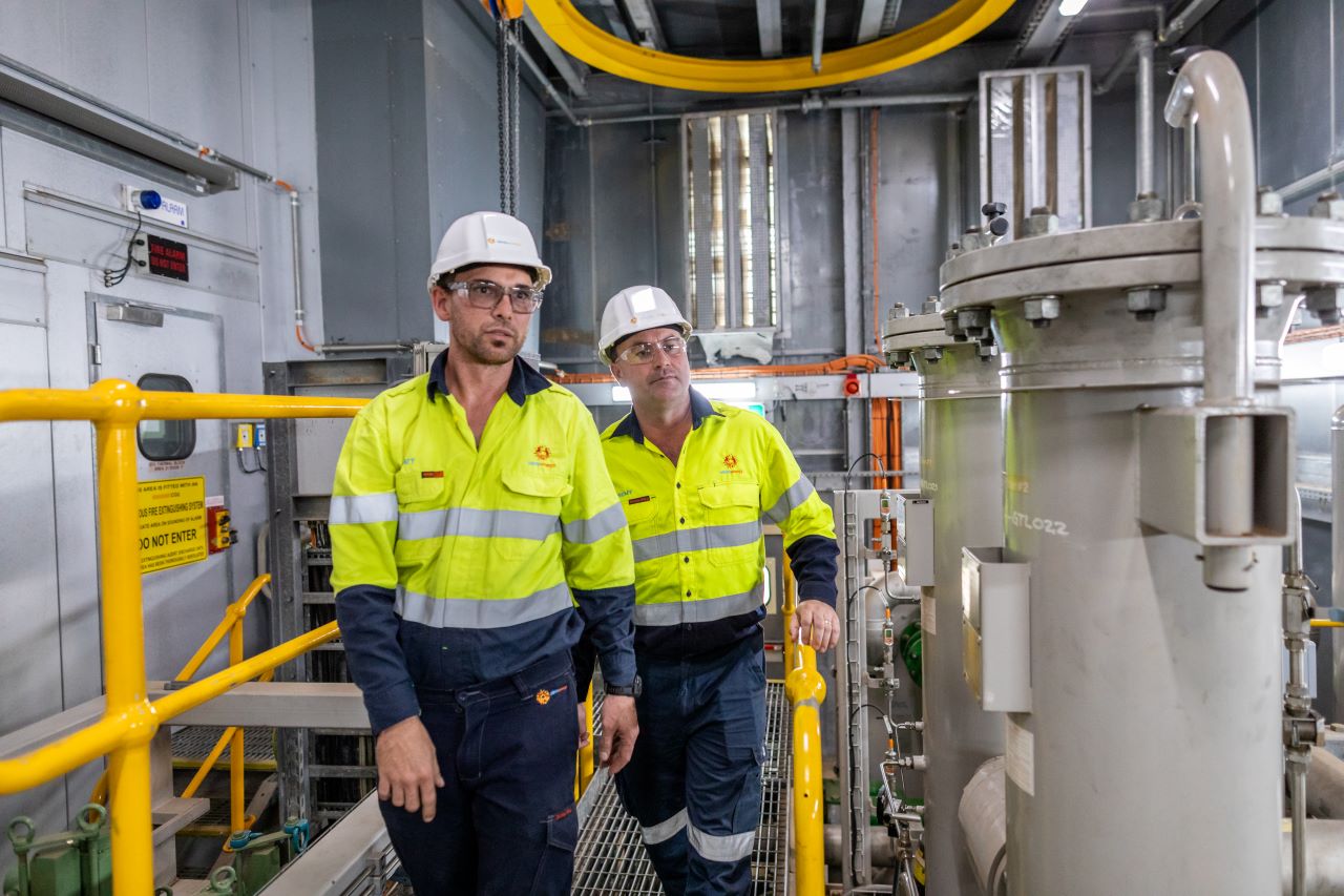 Two workers in hi-vis and hard hats walk through a site.